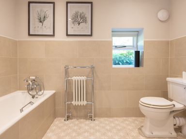 A bathroom with a bathtub on the left a chrome towel radiator in the center a toilet on the right and two framed pictures above the bathtub at Field Head House Graythwaite near Hawkshead