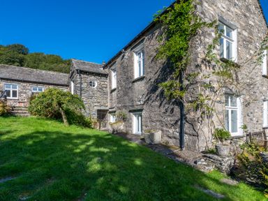 Stone house with white framed windows climbing plants on walls and green lawn at Field Head House in Graythwaite near Hawkshead