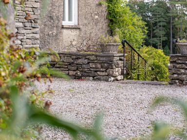 A stone wall with planters overlooking a gravel area and a staircase with black railings at Field Head House in Graythwaite near Hawkshead