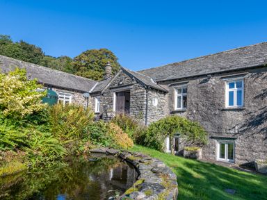 A stone house with white windows and a garden pond at Field Head House in Graythwaite near Hawkshead