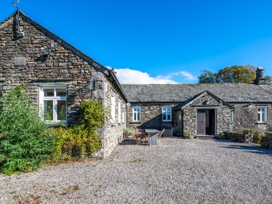 Exterior view of a stone house with several windows gravel yard and outdoor furniture at Field Head House in Graythwaite near Hawkshead
