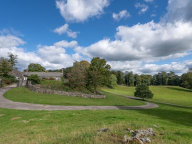 A house with stone walls near a winding road and grassy fields with trees at Field Head House in Graythwaite near Hawkshead