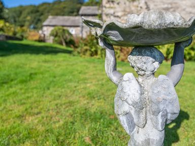 A stone angel birdbath in a garden with grass and stone buildings in the background at Field Head House in Graythwaite near Hawkshead
