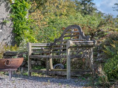 A wooden garden bench near a fire pit and greenery at Field Head House in Graythwaite near Hawkshead