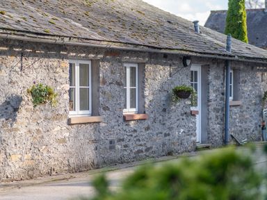 A stone exterior wall with white windows and hanging flower baskets at Grubbings Graythwaite near Hawkshead