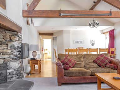 A living room with a brown sofa and red cushions a stone fireplace wooden dining table and chairs at Grubbings Graythwaite near Hawkshead