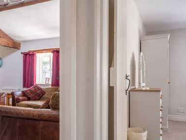 A living room with brown sofas and red curtains next to a bedroom with white furniture at Grubbings Graythwaite near Hawkshead