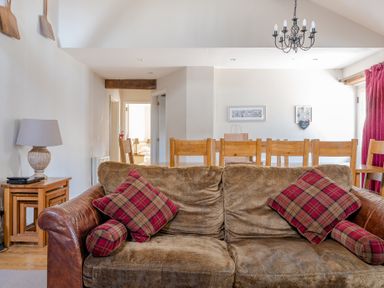 A living room with a brown sofa and plaid pillows in front of a wooden dining table with chairs at Grubbings Graythwaite near Hawkshead