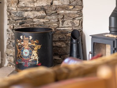 A metal container with a colorful crest design next to a black stove and a stone wall at Grubbings in Graythwaite near Hawkshead