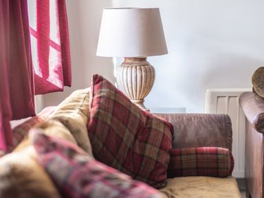 A sofa with plaid pillows and a table lamp next to red curtains at Grubbings Graythwaite near Hawkshead