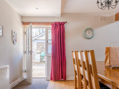 A dining room with wooden chairs and table next to an open door and red curtain at Grubbings Graythwaite near Hawkshead