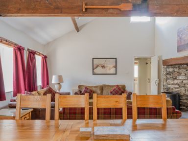 A living room with wooden chairs a wooden table red curtains sofas and a stone fireplace at Grubbings Graythwaite near Hawkshead