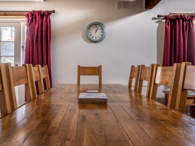 A dining room with a wooden table and chairs a round clock on the wall and red curtains at Grubbings Graythwaite near Hawkshead