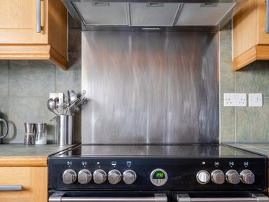 A kitchen stovetop with control knobs and utensils in a container on the counter at Grubbings Graythwaite near Hawkshead