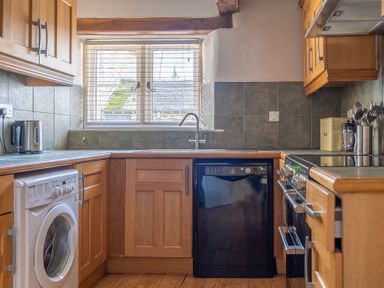 A kitchen with wooden cabinets a washing machine black dishwasher and window blinds at Grubbings in Graythwaite near Hawkshead