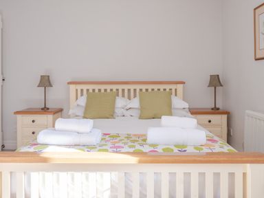 A bedroom with a wooden bed with white sheets green cushions bedside tables with lamps and folded towels on the bed at Grubbings Graythwaite near Hawkshead