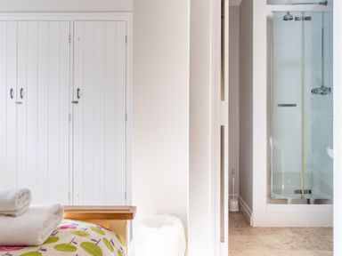 A bedroom with a bed and folded towels next to a white wardrobe and a bathroom with a shower stall at Grubbings in Graythwaite near Hawkshead
