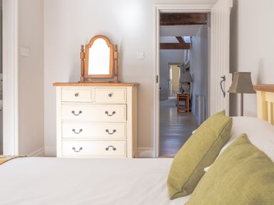 A bedroom with a cream dresser and mirror and green pillows on a bed at Grubbings Graythwaite near Hawkshead