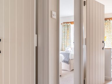A view through doorways into a bedroom with beds towels and patterned curtains at Grubbings Graythwaite near Hawkshead