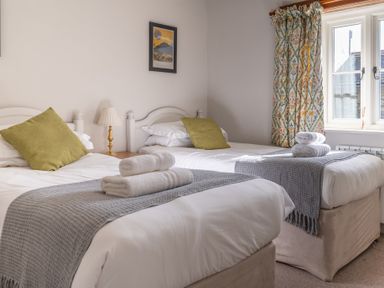 A bedroom with two single beds with green pillows and folded towels on gray throws at Grubbings in Graythwaite near Hawkshead