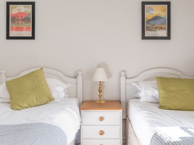 A bedroom with two single beds a bedside table with a lamp and framed pictures on the wall at Grubbings in Graythwaite near Hawkshead