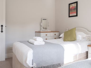 A bedroom with a single bed green pillow and a gray blanket on the bed a dresser with a mirror on top and a framed picture on the wall at Grubbings in Graythwaite near Hawkshead