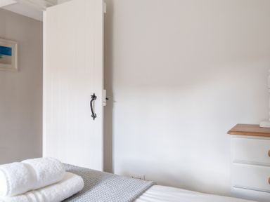 A bedroom with white door partially open a bed with folded white towels and a dresser with wooden top at Grubbings in Graythwaite near Hawkshead
