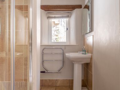 A bathroom with a pedestal sink a wall-mounted mirror a window a metal towel rack and a tiled shower at Grubbings in Graythwaite near Hawkshead