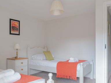 A bedroom with two single beds an orange throw and folded white towels a bedside table with a lamp a framed picture and a hanging light at Grubbings Graythwaite near Hawkshead