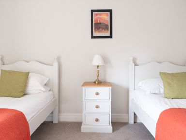 A bedroom with two white single beds, a white nightstand with a lamp, and a framed picture on the wall at Grubbings Graythwaite near Hawkshead