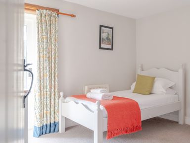 A bedroom with a single white bed with a green pillow and red blanket near a window with floral curtains at Grubbings Graythwaite near Hawkshead
