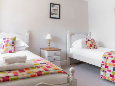 A bedroom with two single beds a bedside table with a lamp and colorful pillows and blankets at Grubbings in Graythwaite near Hawkshead
