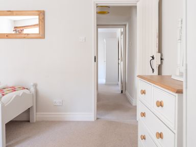 A bedroom with a white bed frame a dresser and a wooden framed mirror at Grubbings in Graythwaite near Hawkshead