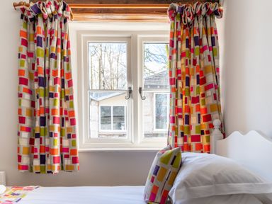 A bedroom window with colorful patterned curtains and a bed with a matching cushion at Grubbings Graythwaite near Hawkshead