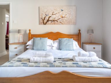 A bedroom with a wooden bed frame two blue pillows white towels on the bed two bedside tables with lamps and a painting of birds on a branch above the bed at Grubbings in Graythwaite near Hawkshead