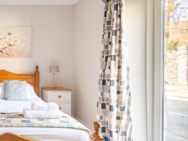 A bedroom with a wooden bed white towels on the bed a bedside table with a lamp and patterned curtains at Grubbings Graythwaite near Hawkshead