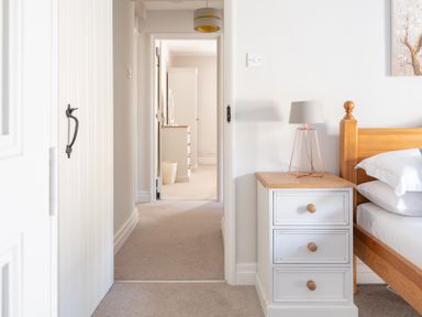 A bedroom with a wooden bed a white bedside table with a lamp and a view into a hallway with furniture at Grubbings Graythwaite near Hawkshead