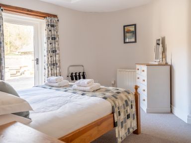 A bedroom with a double bed folded towels a chest of drawers with a mirror and a door with curtains at Grubbings Graythwaite near Hawkshead