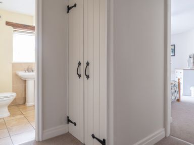 A hallway with a closed cupboard between a bathroom with a toilet and sink and a bedroom with a bed and dresser at Grubbings Graythwaite near Hawkshead