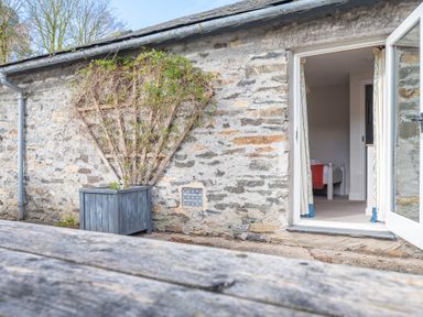 Stone wall with a planter box holding a vine and an open door showing a bedroom at Grubbings Graythwaite near Hawkshead