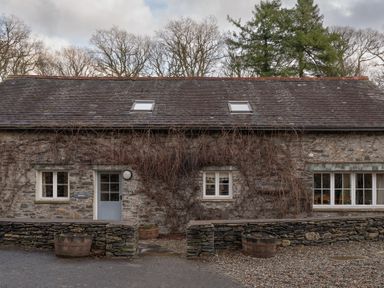 Stone cottage with a gray door and windows with vines on the facade and barrel planters at Bull Pen in Graythwaite near Hawkshead