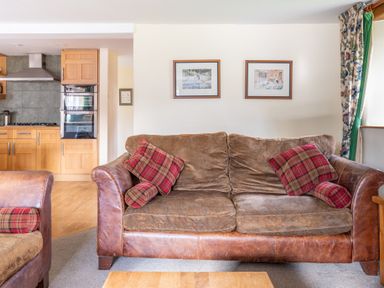 A living room with a brown sofa and red plaid cushions next to a kitchen with wooden cabinets at Bull Pen Graythwaite near Hawkshead
