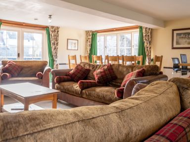 A living room with brown sofas and plaid cushions near a wooden dining table with chairs at Bull Pen in Graythwaite near Hawkshead