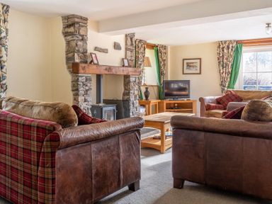 A living room with leather and fabric sofas a wooden coffee table a stone fireplace and a TV at Bull Pen in Graythwaite near Hawkshead