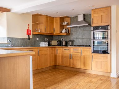 A kitchen with wooden cabinets and drawers a sink toaster microwave kettle oven and stove at Bull Pen Graythwaite near Hawkshead