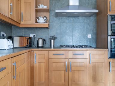 A kitchen with wooden cabinets a gas stove a stainless steel kettle a microwave toaster and kitchen utensils at Bull Pen Graythwaite near Hawkshead