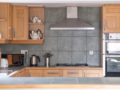 A kitchen with wooden cabinets a stove a stainless steel hood a kettle a microwave and kitchen utensils at Bull Pen in Graythwaite near Hawkshead