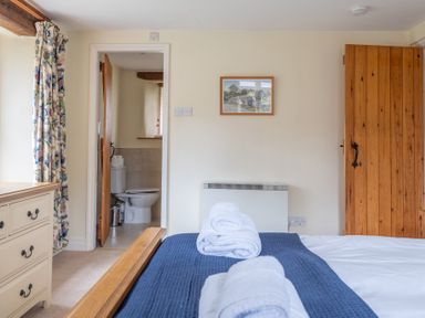A bedroom with a bed and rolled towels next to an open door leading to a bathroom at Bull Pen in Graythwaite near Hawkshead