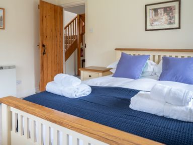 A bedroom with a bed towels pillows wooden door bedside table and staircase at Bull Pen Graythwaite near Hawkshead