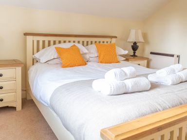 A bedroom with a bed with orange pillows white towels and two bedside tables with lamps at Bull Pen in Graythwaite near Hawkshead